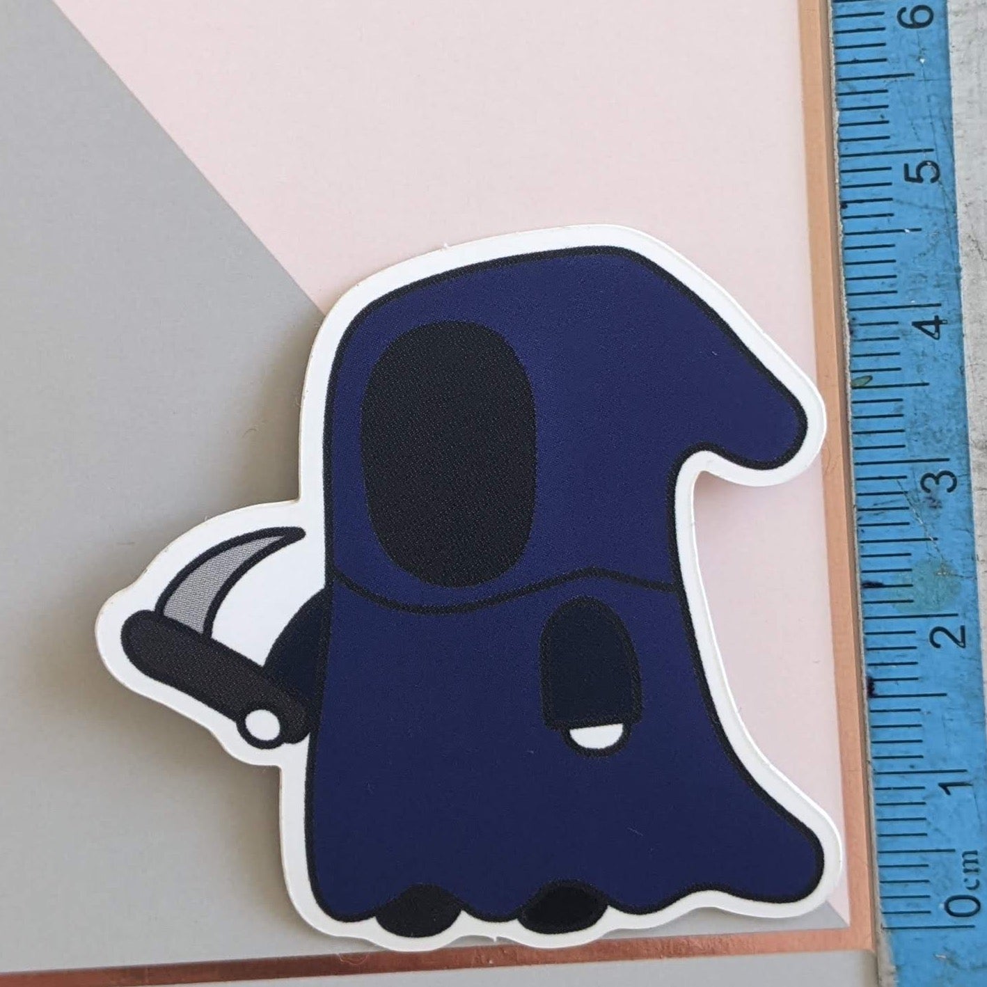 A close up of the grim boi sticker with a ruler showing the scale at 4.5cm tall