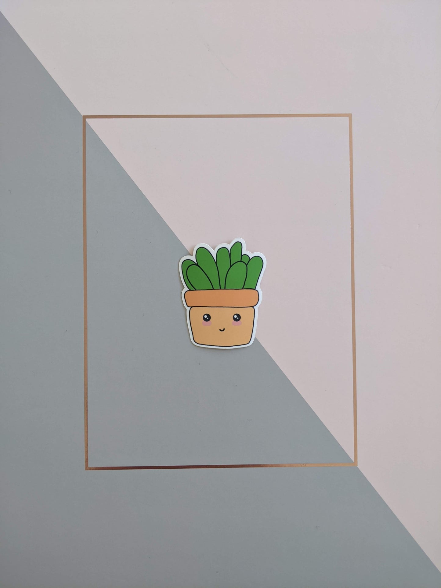 A cute succulent sticker on a pink and grey background. He has a squarish looking light orange pot with a smiley face and blushed cheeks. Chunky grass green leaves sprout from the top of the pot.