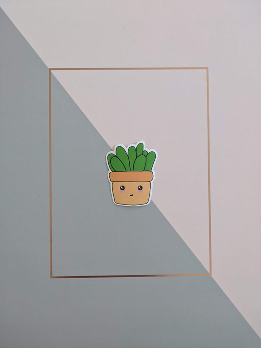 A cute succulent sticker on a pink and grey background. He has a squarish looking light orange pot with a smiley face and blushed cheeks. Chunky grass green leaves sprout from the top of the pot.