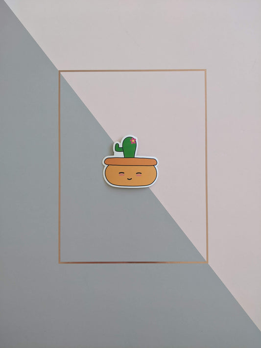 A cactus plant sticker on a pink and grey background. it has a  bowl shaped light orange pot with a closed eyes smiley face and blushed cheeks. Growing out of the pot is a small green cactus with one arm and a little pink flower.